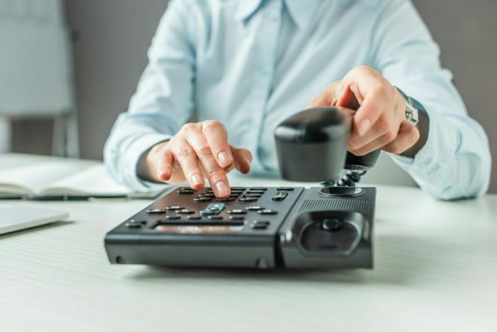 Cropped view of businesswoman with handset dialing number on landline telephone at table on blurred